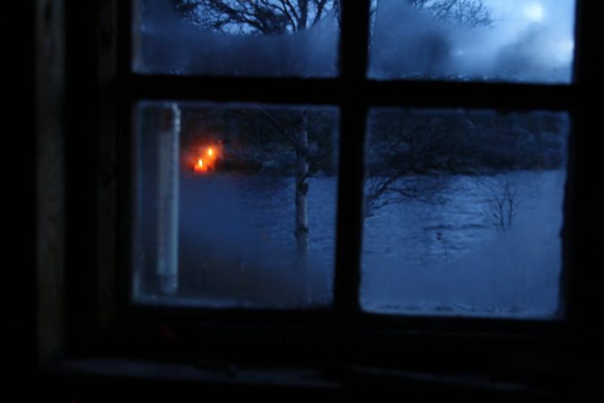 Večerní výhled z útulné chaty do večerní zimy.