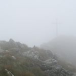Z mlhy se vynořuje vrcholový kříž Hochrettelsteinu.
